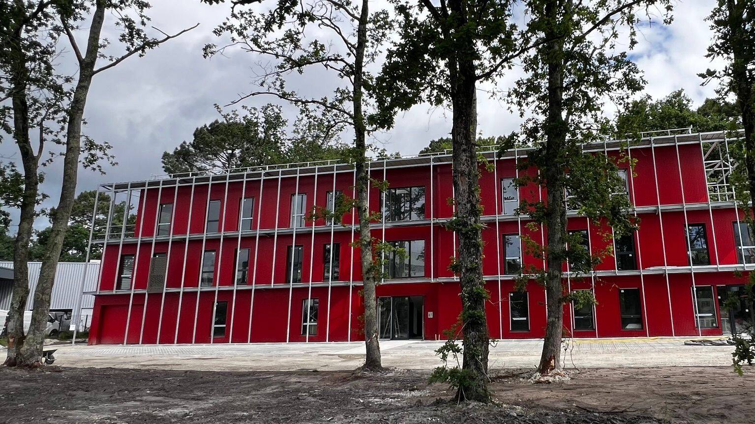 Le bâtiment de l'Espace Galilée, une façade rouge rythmée de fines structures blanches, au milieu des arbres